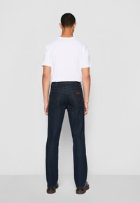 Jeans de mezclilla azul oscuro con corte de pierna recta, cinco bolsillos y una placa de cuero en la pretina trasera; combinados con una camiseta blanca lisa.