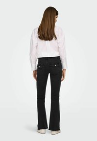 Sorte flared jeans med høj talje og baglommer, kombineret med en hvid skjorte med knapper, lange ærmer og en afrundet kant.