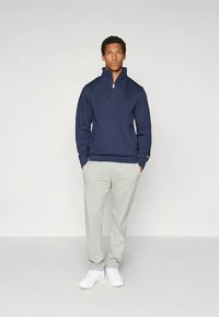 Sudadera con cremallera azul marino y cuello alto, combinada con pantalones deportivos grises y zapatillas blancas. Tela suave, diseño sencillo, sin estampados ni adornos.