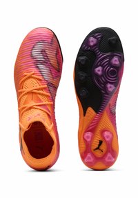 Kirkkaan oranssit ja vaaleanpunaiset jalkapallokengät, joissa on teksturoitu päällinen, nauhallinen malli ja erottuva monivärinen pohja, jossa on nastat ja brändäys.