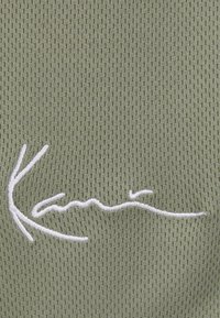 Olive green knit fabric features a textured pattern with a prominent white embroidered logo, showcasing a smooth, flowing design.