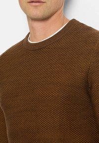 Brauner strukturierter Pullover mit rundem Ausschnitt und dezentem Muster, der eng um den Kragen und die Schultern sitzt.