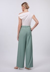 Light beige off-the-shoulder top paired with high-waisted, wide-leg mint green trousers. Smooth fabric and elastic waistband with back pockets.