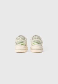 Para jasnobeżowych i zielonych sneakersów New Balance 1000, pokazane od tyłu na jednolitym białym tle.