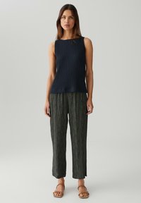 Top senza maniche a costine blu navy abbinato a pantaloni a gamba larga verdi con un motivo a foglie e una vestibilità comoda. Sandali neutri completano il look.