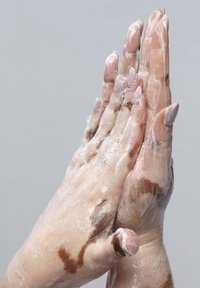 Rengöring av händer med synliga bubblor från tvål; ena handen är ljusare i färgen med nagellack, den andra har mörkare mönster och kortare naglar.