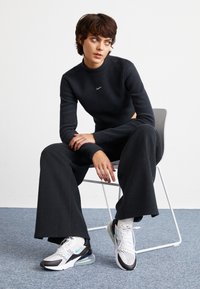 Svart stickad långärmad topp med en liten Nike-logotyp, parat med lösa svarta vida byxor och vita sneakers med svarta och teal-accenter.