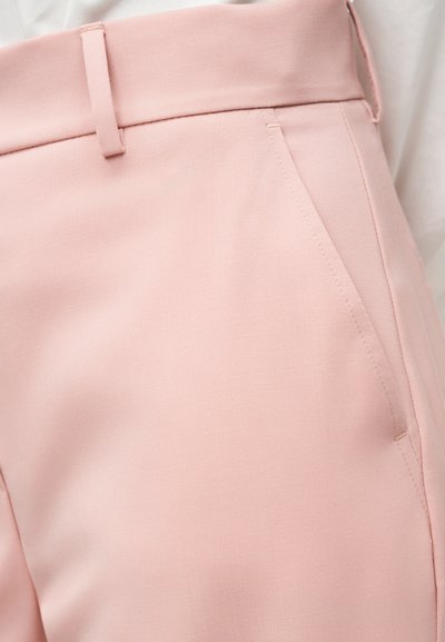 Κοντινό πλάνο ανοιχτόροζ ραμμένων παντελονιών που δείχνει τη μέση, την θηλιά της ζώνης και λεπτομέρειες πλαϊνής τσέπης σε λείο ύφασμα.