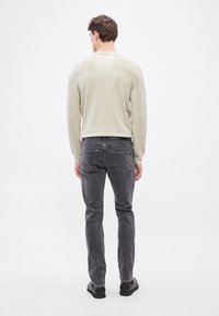 Μπεζ ανοιχτό μπεζ πλεκτό πουλόβερ με μακρύ μανίκι και ριμπ ύφασμα, συνδυασμένο με σκούρα γκρι τζιν στενής εφαρμογής. Απλός σχεδιασμός, ελάχιστες λεπτομέρειες και μονόχρωμα χρώματα.