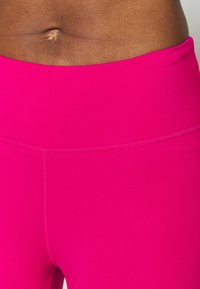 Dopasowane legginsy sportowe w jaskrawym różowym kolorze, wykonane z gładkiego materiału i szerokiego pasa, z delikatnymi detalami szwów.