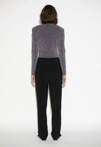 Graue, strukturierte Langarm-Bluse mit hohem Kragen; kombiniert mit schwarzen, maßgeschneiderten, geraden Hosen. Rückansicht.