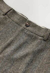Gray and brown houndstooth fabric with a flat front, featuring a single brown button closure and neatly folded waistband.