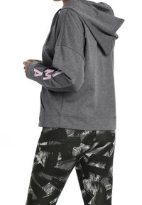 Šedá mikina s kapucí a růžovým nápisem na pravém rukávu, spárovaná s legínami s černobílým abstraktním vzorem. Měkká tkanina, volný střih.