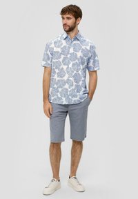 Korte mouwen shirt met een blauw-wit bladerenpatroon, gecombineerd met lichtgrijze shorts. Model draagt witte sneakers met zwarte accenten.