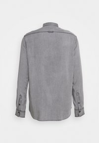 Chemise en denim gris à manches longues avec poignets boutonnés, coutures visibles et petit détail de l'empiècement arrière, vue de dos sur fond blanc.