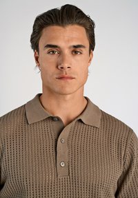 Beige stickad polo med ett strukturerat mönster, med krage och tre knappar, designad för en figurnära passform.