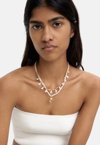 Naszyjnik warstwowy z białymi koralikami, złotymi akcentami i muszelkowymi zawieszkami. Teksturowe materiały tworzą unikalny, wielotonowy wzór.