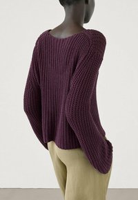 Maglione lavorato a maglia di un viola scuro, con una vestibilità ampia, spalle scese e texture a coste. Abbinato a pantaloni chiari per un contrasto.