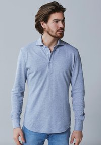Lange mouwen polo-shirt in lichtgrijs, gemaakt van zachte stof, met een twee-knops sluiting en een klassieke kraag; gedragen met blauwe jeans.