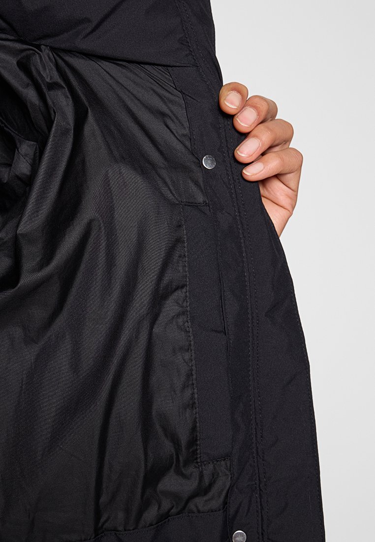 Inneres einer schwarzen Daunenjacke mit strukturierter Fütterung, Druckknopfdetail und Stofftasche. Weiches, glattes Material mit leichtem Glanz.