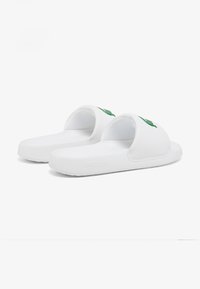 Witte rubberen slip-on sandalen met een open teen ontwerp, voorzien van een groen Lacoste-logo op de band en een gestructureerde voetbed voor grip.