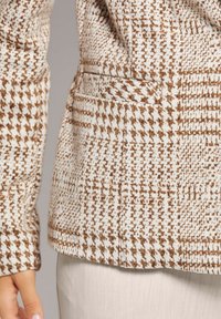 Bruin en wit houndstooth-patroon jack met een gestructureerde stof, voorzien van een zijzak en gedetailleerde kraag.