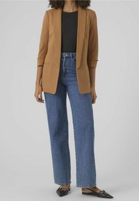 Brązowa marynarka z klapami, zestawiona z niebieskimi dżinsami o wysokim stanie i szerokimi nogawkami oraz czarnymi, spiczastymi balerinami. Gładki materiał i dopasowany krój.