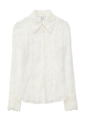Weiße Spitzenbluse mit langen Ärmeln, Knopfleiste vorne und Kragen. Verziert mit zarten Blumenmustern und gezackten Spitzenmanschetten.