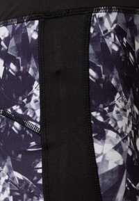Schwarze hochgeschnittene Leggings mit einem seitlichen Paneel im Diamantmuster in Grautönen und Weiß, mit strukturierten Nähdetails.