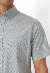 Kurzärmliges Hemd mit Button-Down-Kragen in einer hellblauen Grundfarbe und dunklem blauen geometrischen Muster. Es hat einen umgelegten Kragen und weiße Knöpfe.