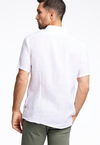 Korte mouwen, achteraanzicht van een lichtgewicht, witte linnen shirt. Kenmerkt zich door een kraag en een ontspannen pasvorm met zijsplitten.