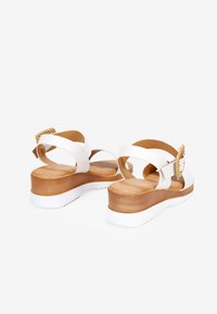 Sandalias de plataforma blancas con correas cruzadas, un tacón de aspecto de madera y un acento decorativo de trenzado dorado en la parte trasera.