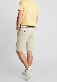 Pantaloni corti beige chiaro con una vestibilità rilassata, dotati di tasche frontali, una cintura a righe a contrasto e una texture in cotone morbida.