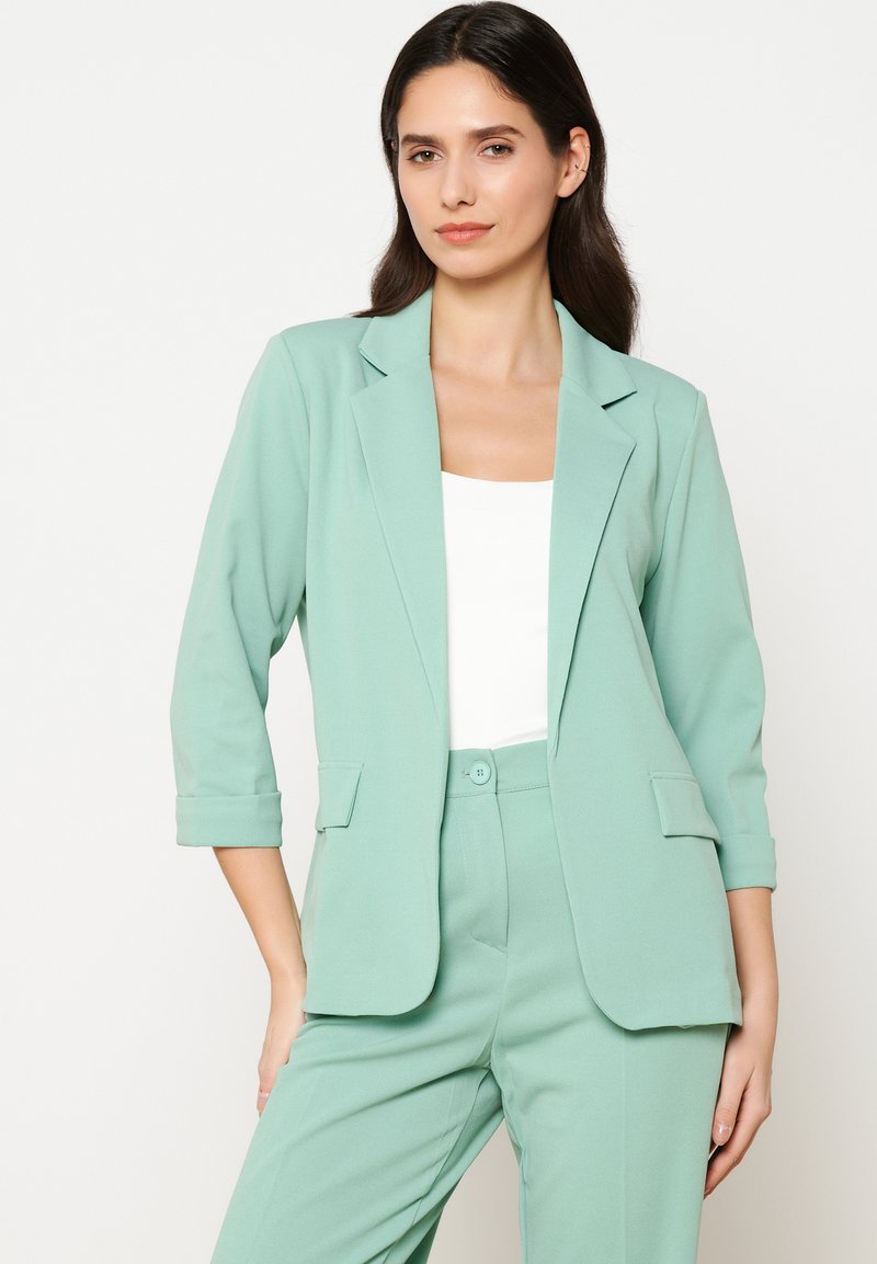 Mėtinės žalios spalvos bleiseris su įpjovimu ant apykaklės, dviem priekinėm kišenėm ir trijų ketvirčių rankovėm, pagamintas iš lygaus, lengvo audinio.