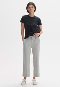 Black cotton t-shirt, light gray relaxed-fit trousers with drawstring, and white sneakers. A small black quilted bag is held on the side.