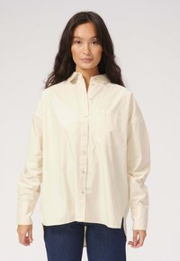 Cremefarvet skjorte med knapper i letvægtsbomuld, med en brystlomme, lange ærmer og en afrundet kant med sideslidser.