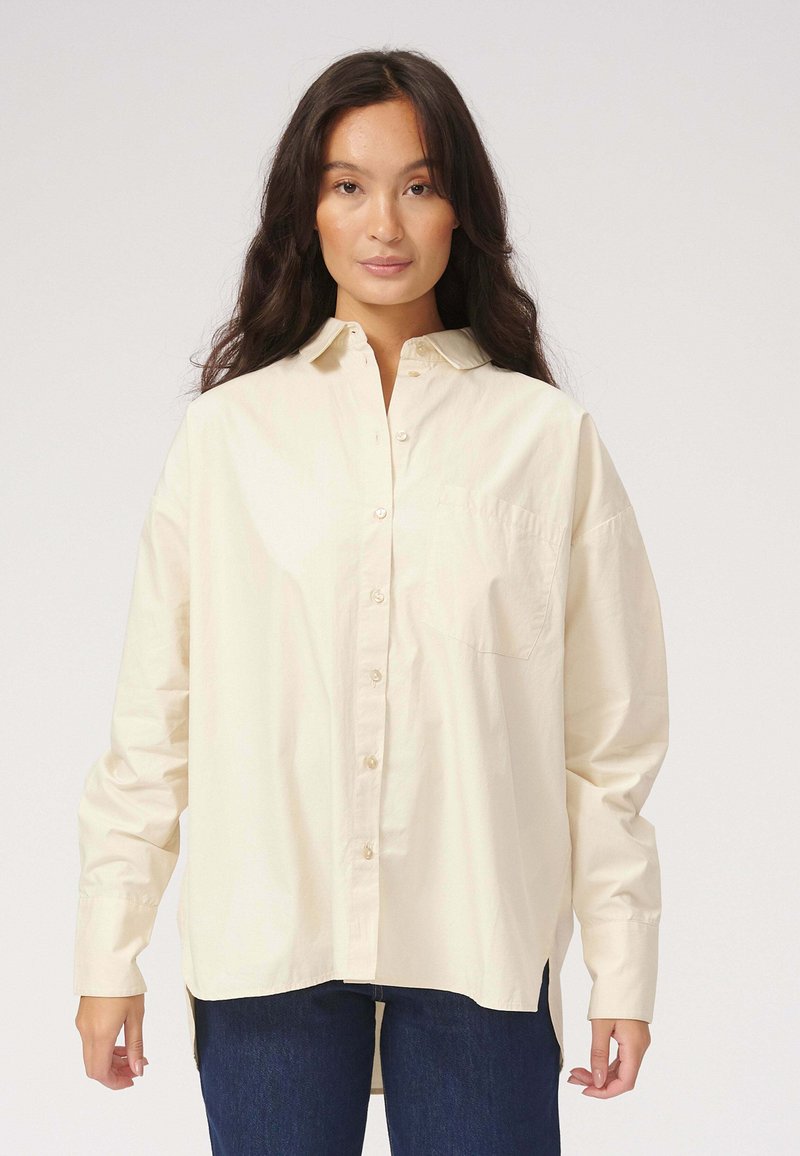 Cremefarvet skjorte med knapper i letvægtsbomuld, med en brystlomme, lange ærmer og en afrundet kant med sideslidser.