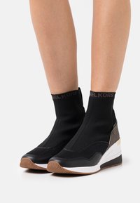 Botines de punto negros con puntera de cuero liso y suela de goma blanca, con un patrón texturizado y una sutil marca en el puño.