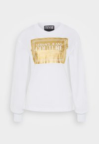 Bílé tričko s dlouhým rukávem, které na přední straně zdobí velký zlatý fóliový logotyp, s ribbovanými manžetami a kulatým výstřihem. Měkká bavlněná tkanina.