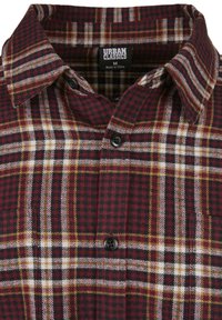 Rot-schwarzes Karohemd mit einem Knopfkragen, zwei schwarzen Knöpfen sowie weißen und gelben Akzenten in einem gewebten Stoff.