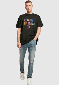 Sort t-shirt med farverig tekst, der står "HATE IT OR LOVE IT," kombineret med slidte lyseblå jeans og hvide sneakers.