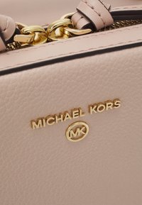 Sac en cuir rose clair avec une finition texturée, quincaillerie dorée et logo "Michael Kors" en relief avec un accent circulaire "MK".