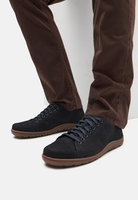 Adidași negri din suede au un design low-top, vârf rotund, un sistem de șireturi proeminent și o talpă din cauciuc texturată cu accente maro.