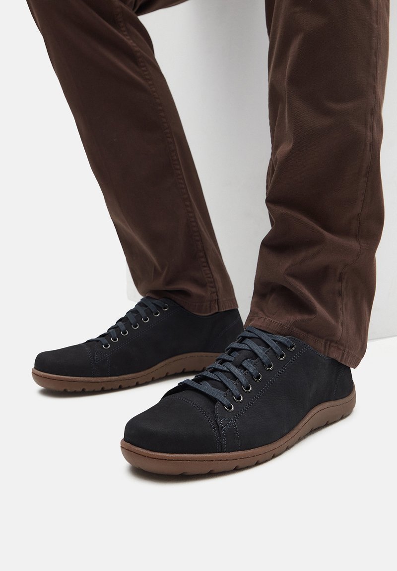 Adidași negri din suede au un design low-top, vârf rotund, un sistem de șireturi proeminent și o talpă din cauciuc texturată cu accente maro.