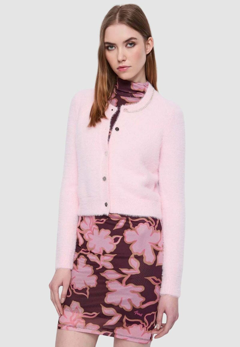 Cardigan rosa fluffy con maniche lunghe, scollo tondo e bottoni decorativi, abbinato a una gonna fitted con motivo floreale in colori scuri.