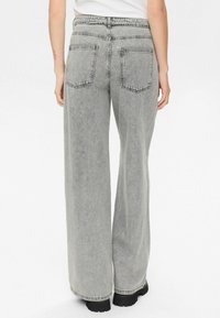 Jean en denim gris à jambes larges avec une finition délavée, comprenant deux poches arrière, une taille haute et de robustes semelles noires visibles au niveau de l'ourlet.