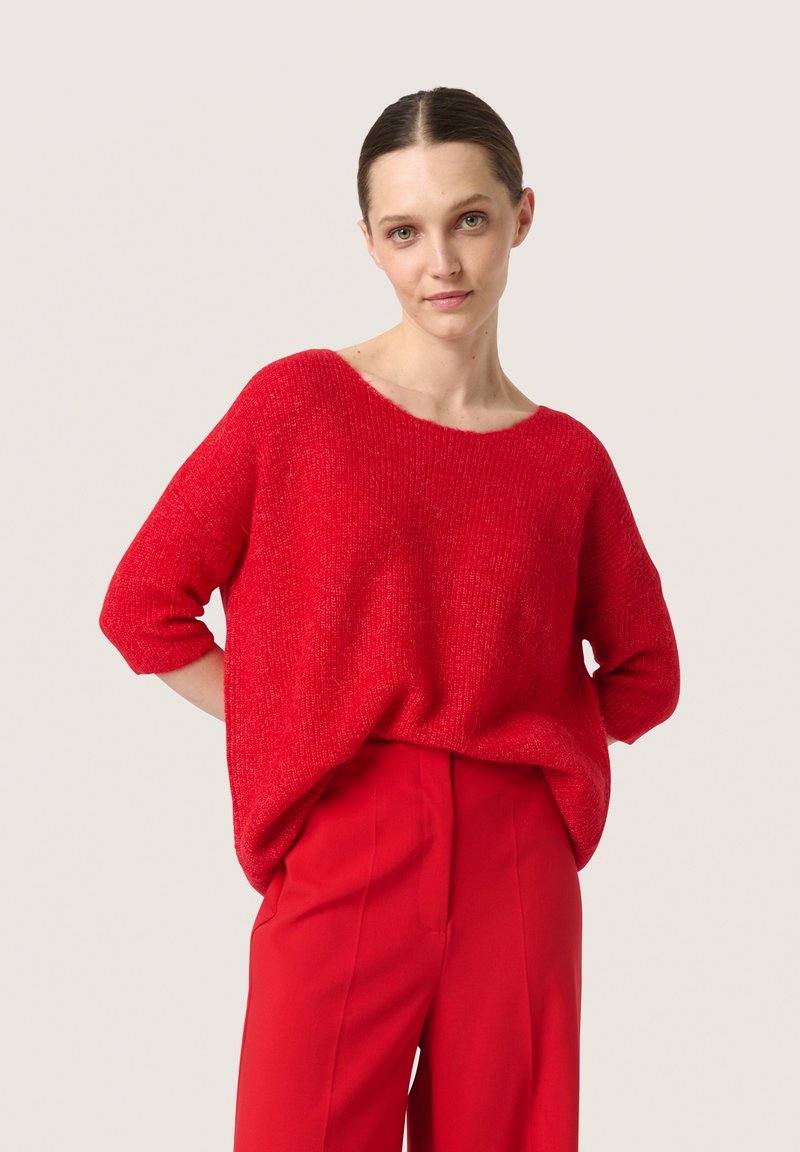 Rød strikket sweater med løs pasform, rund halsudskæring og korte ærmer, sat sammen med røde skræddersyede bukser. Den strukturerede stof giver dybde.