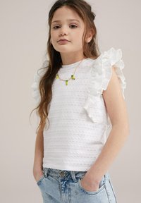 Bílý bavlněný top s volánovými rukávy, texturovaný malými oky. V kombinaci se světle modrými džínovými šortkami s květinovou výšivkou.