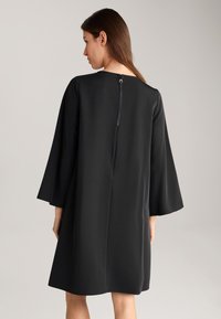 Zwarte jurk met een losse pasvorm, lange klokmouwen en een rits aan de achterkant. Soepele textuur en knielange uitstraling.