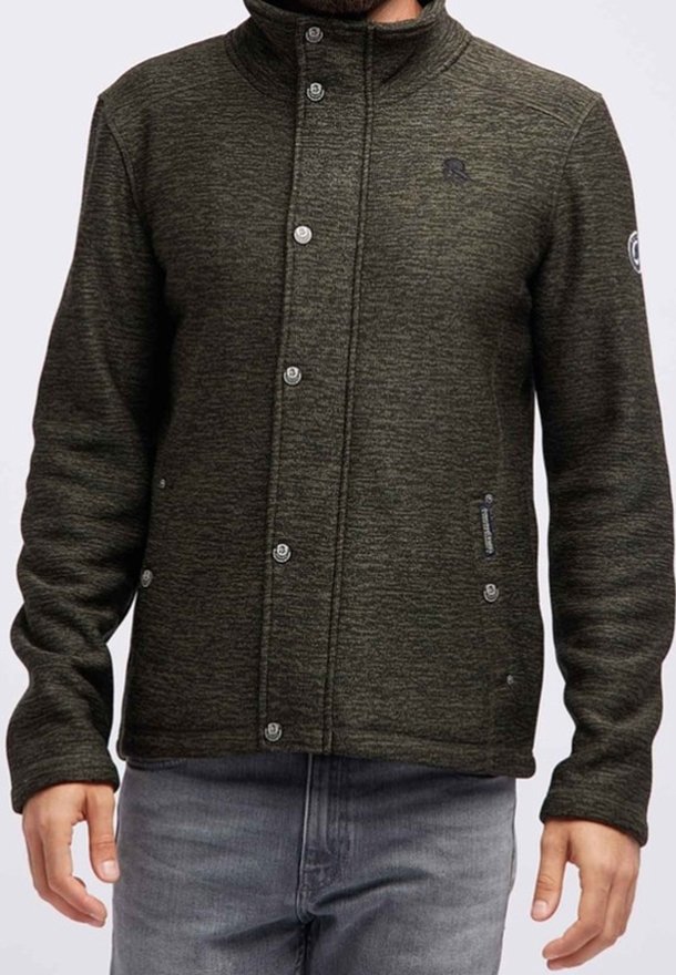 Uomo che indossa una giacca in maglia verde scuro con zip e bottoni a pressione, due tasche frontali e un logo sul petto e sulla manica.